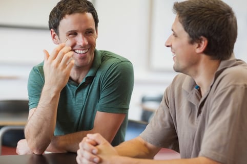 Two friendly male mature students chatting while sitting in class room